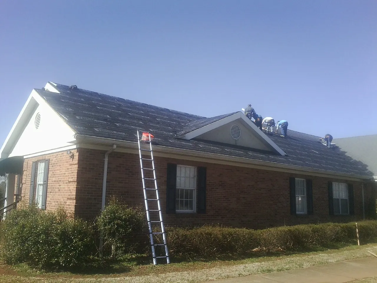 Crew tearing shingles off a brick ranch roof with a ladder set — Metal Roof Repair work by our crew in Norwich
